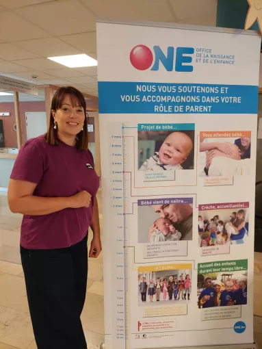 La représentante de l'ONE qui pose devant un roll-up d'informations de l'ONE