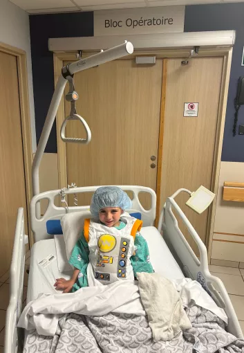 Enfant en tenue d'astronaute dans un lit d'hôpital souriant à l'appareil photo. Devant le bloc opératoire