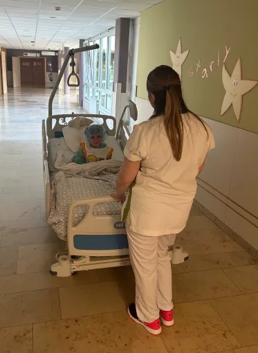 Petit patient dans un lit d'hôpital en direction du bloc opératoire avec une infirmière de dos qui pousse le lit