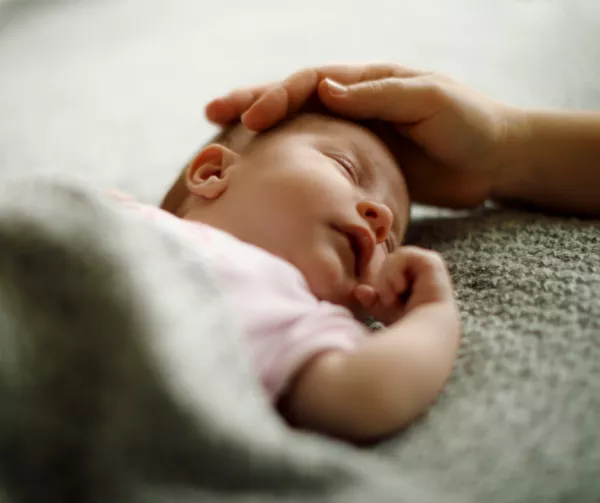 Bébé couché avec une couverture sur lui. une main adulte est posée sur sa tête